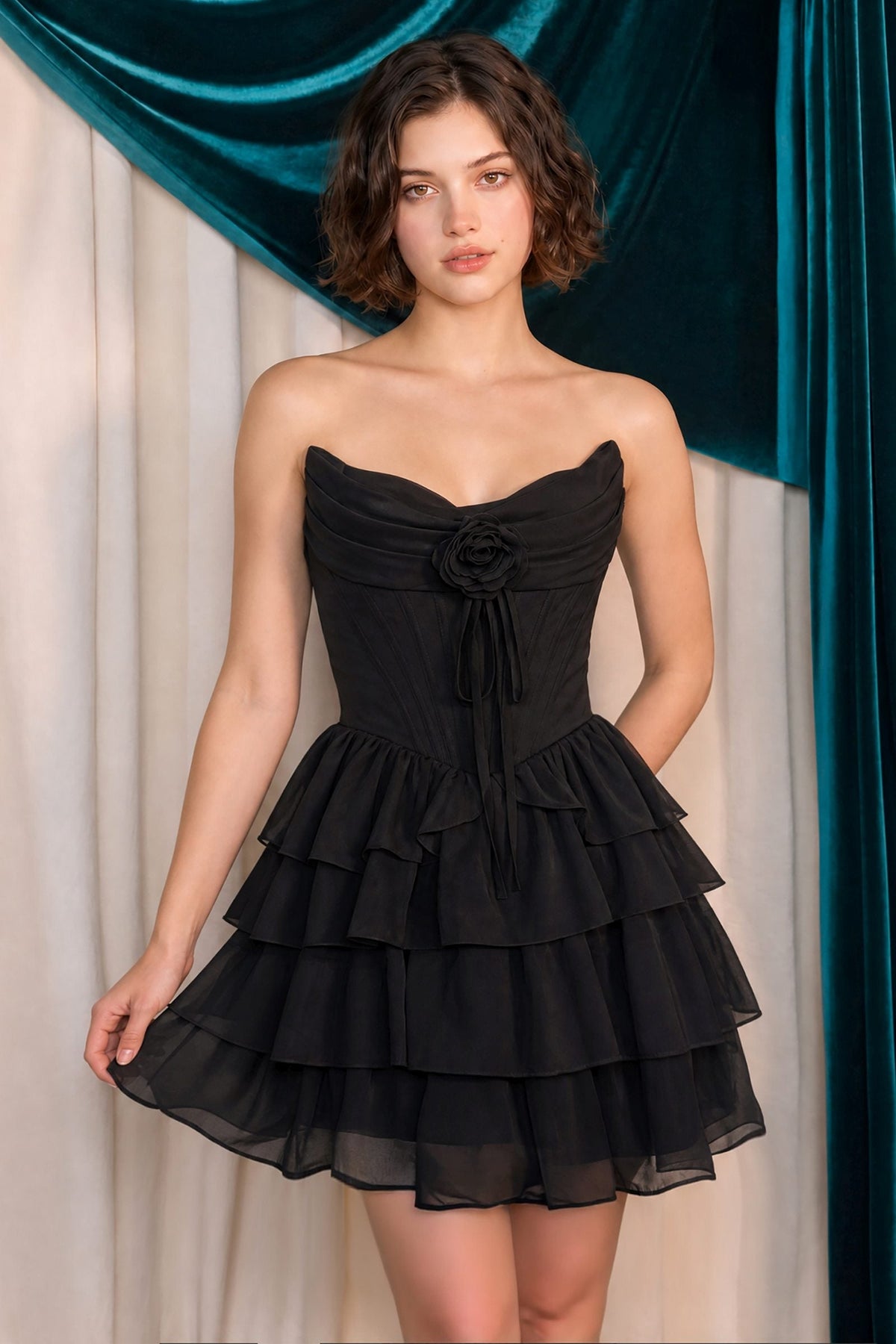 Woman wearing a black strapless dress with ruffled layers against a teal curtain background