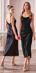 Two women wearing black satin slip dresses in a room with wooden flooring and white walls.
