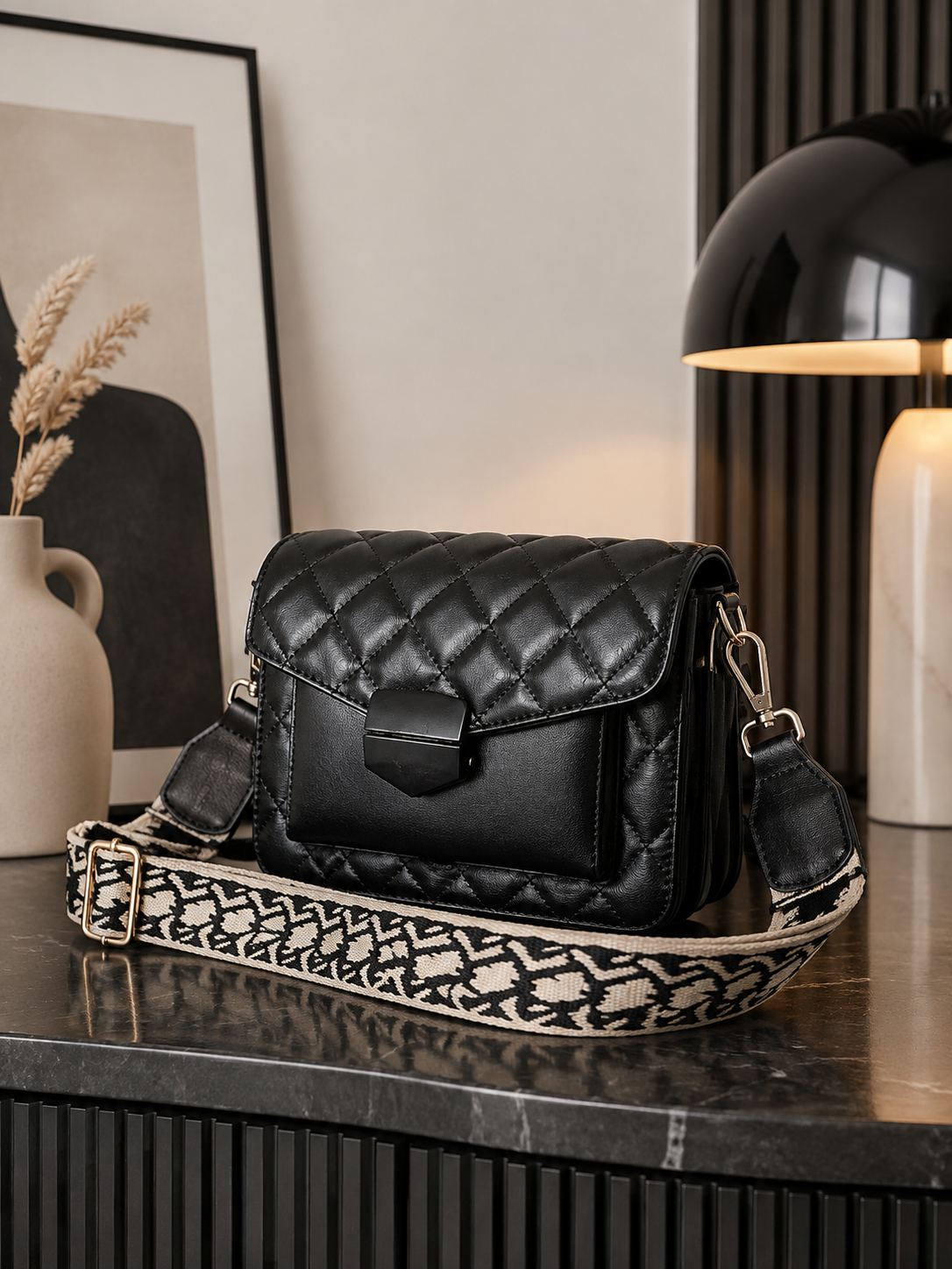 A black quilted leather shoulder bag with a patterned woven strap, displayed on a dark marble tabletop in a modern interior setting-BlackOrvani