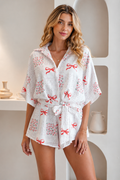 A woman modeling a white short-sleeve romper with a red bow and floral print, standing in a brightly lit, modern interior setting-BlackOrvani