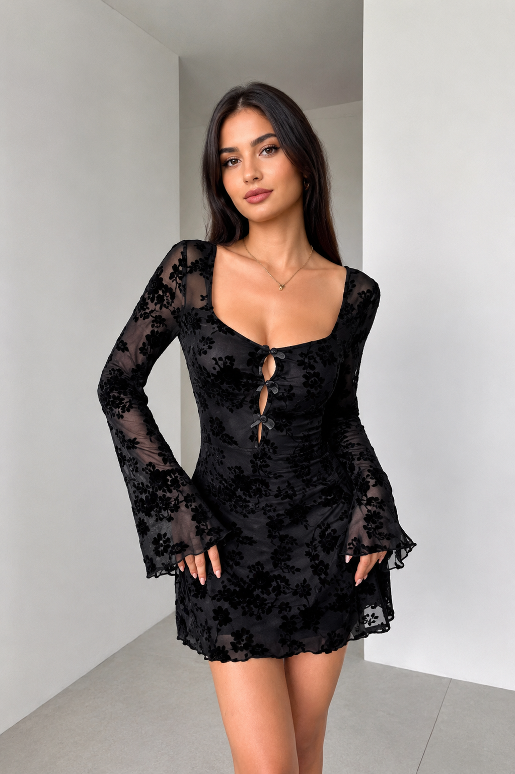A woman modeling a black sheer floral lace mini dress with long flared sleeves, a scoop neckline, and a front keyhole cutout with ties-BlAcKORvAni
