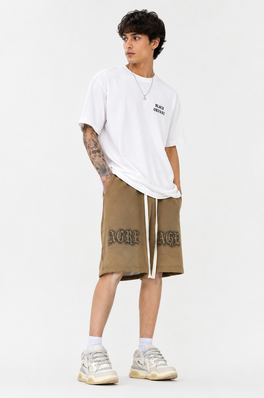 Men’s oversized white T-shirt paired with khaki drawstring shorts featuring bold graphic lettering, white socks, and chunky sneakers, styled in a clean modern streetwear look.Black orvani