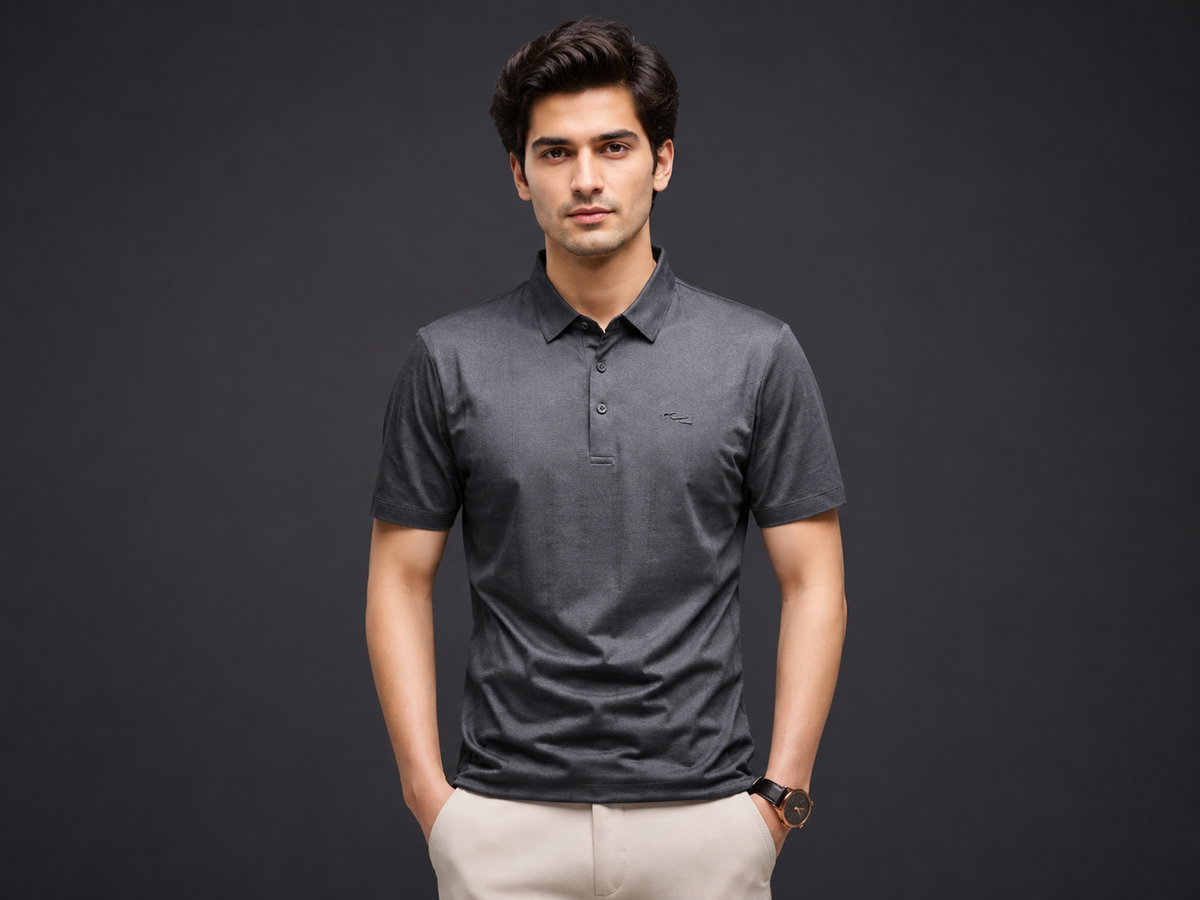 A man wearing a dark gray short-sleeve polo shirt and beige trousers, standing against a dark gray studio background-blackorvani