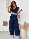 A woman models a navy blue wide-leg jumpsuit with a gold embroidered waistband, styled with a small woven bag and white heeled sandals in a bright, modern room setting-BlackOrvani