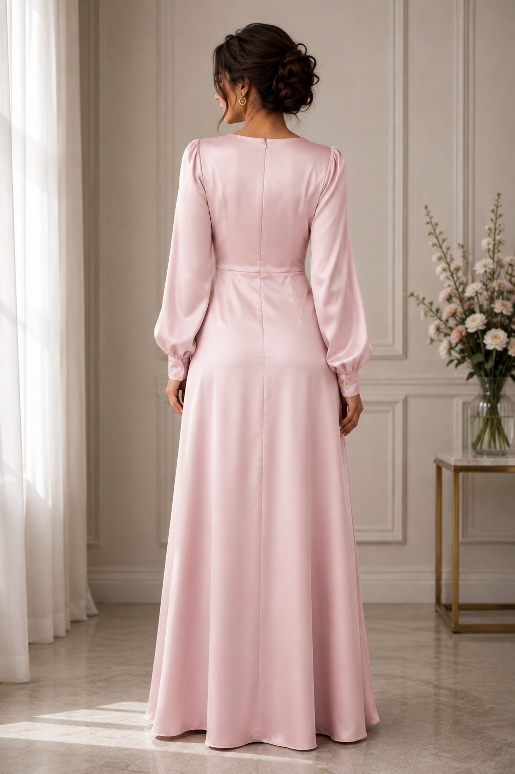 A woman viewed from behind wearing a long, floor-length pink dress with long sleeves and a fitted waist, standing in a softly lit indoor room with curtains and a side table with flowers-BlackOrvani