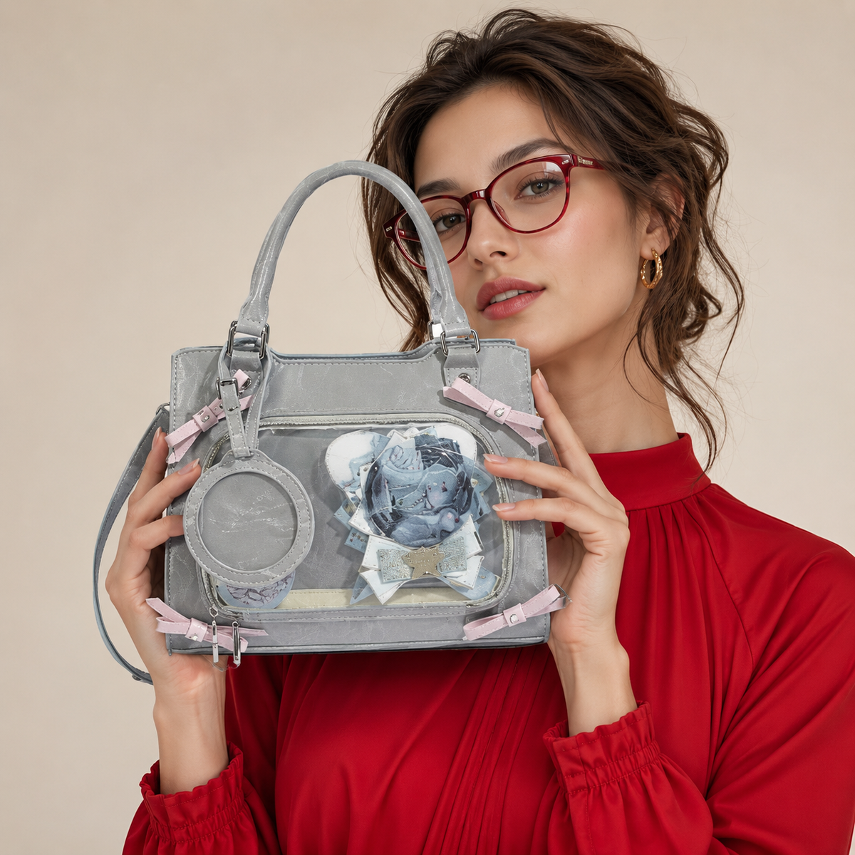 A  light gray structured handbag with a clear front window, pink ribbon accents, and a circular charm, hold by a women -BlackOrvani