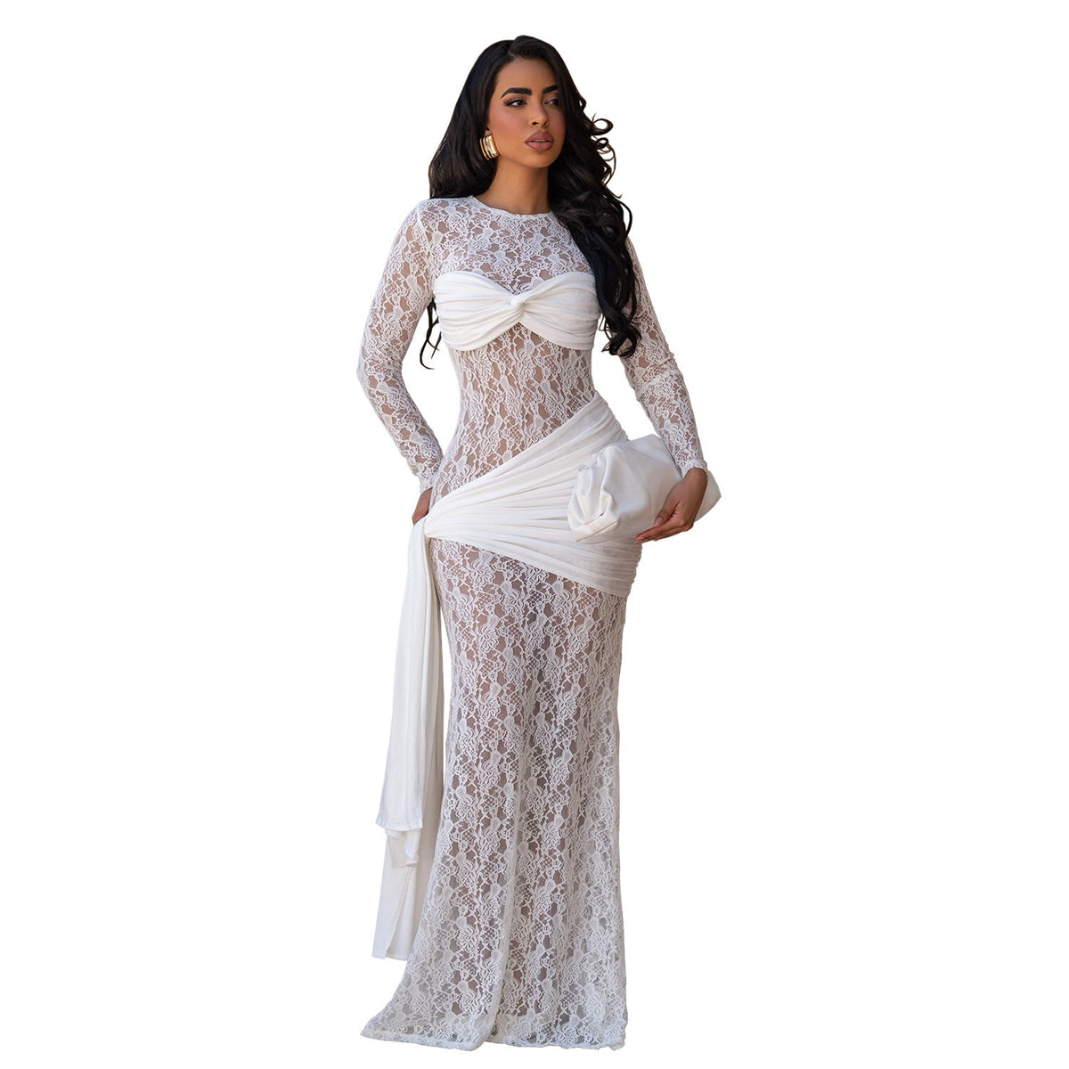 A woman modeling a long-sleeve white lace maxi dress with a sweetheart neckline, a twisted front detail, and a draped sash at the waist, shown against a plain white background.