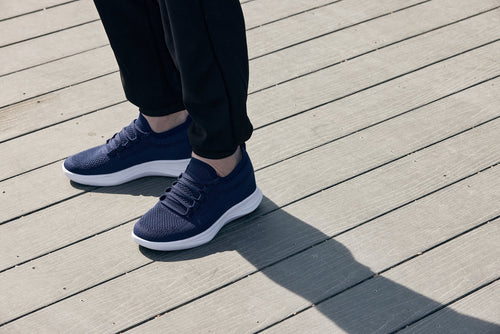 Navy blue sneakers worn on a wooden deck-blackorvani