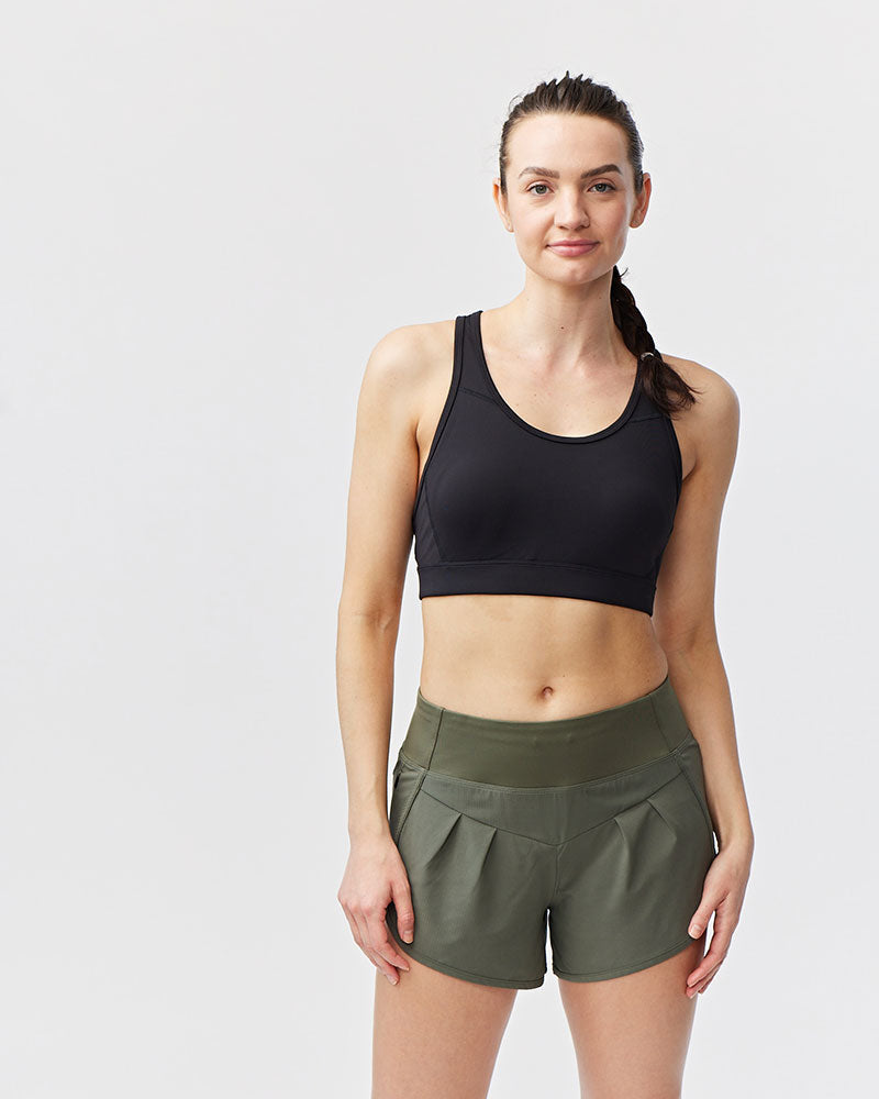 Woman wearing a black sports bra and green shorts on a white background