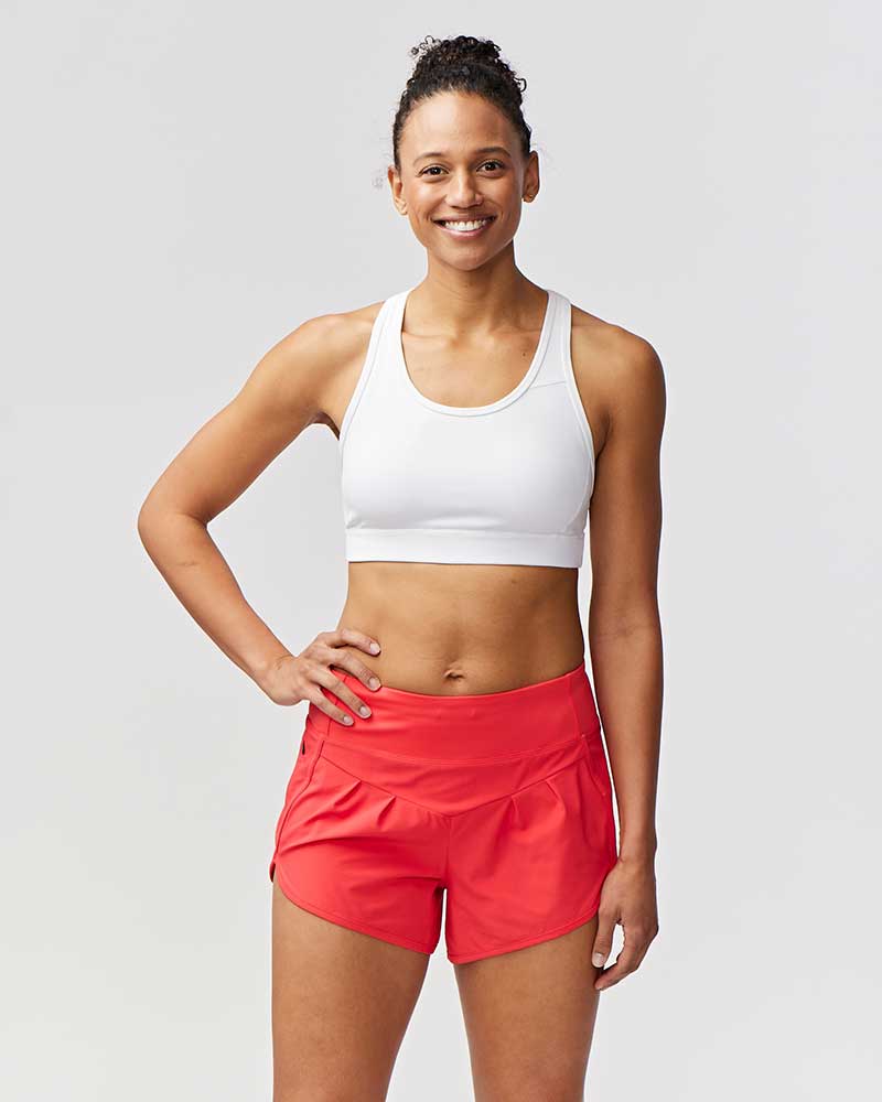 Woman wearing a white sports bra and red shorts on a light gray background