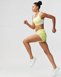 Woman in yellow athletic outfit running on a light gray background