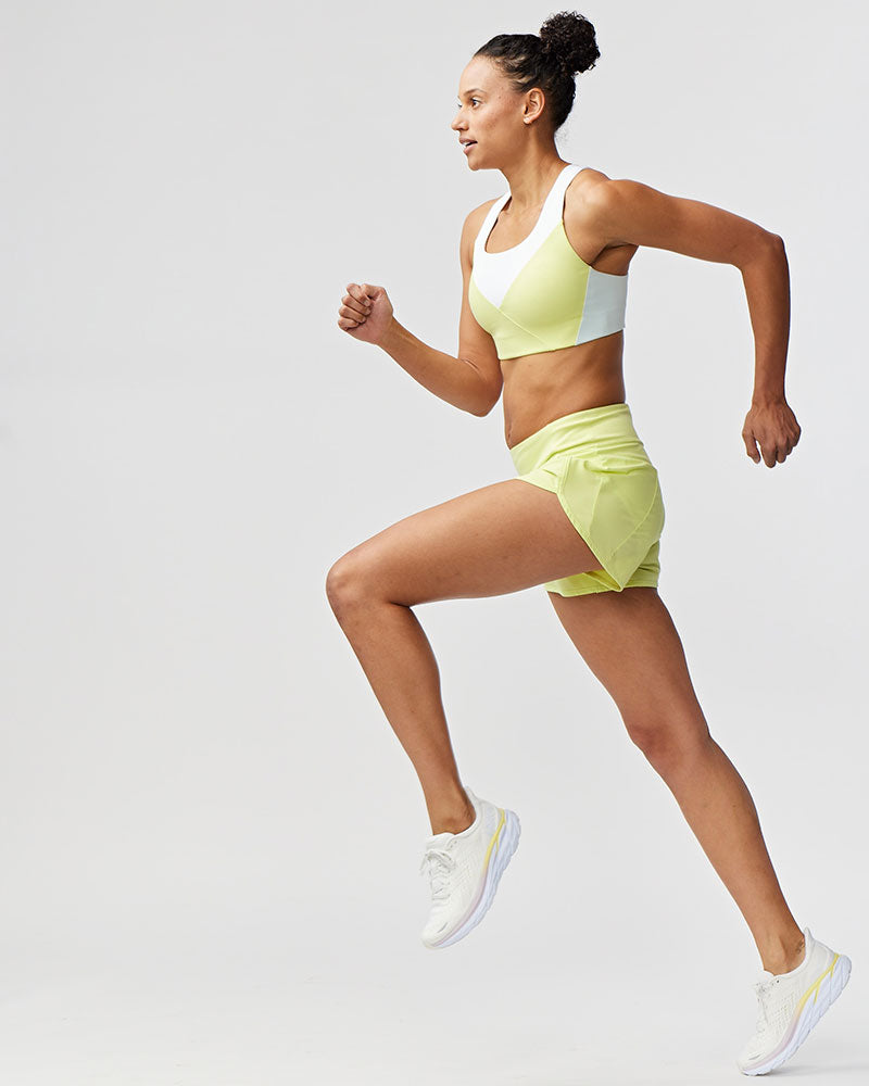 Woman in yellow athletic outfit running on a light gray background