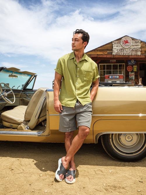 Man standing next to a vintage car in a desert setting with a building in the background-blackorvani