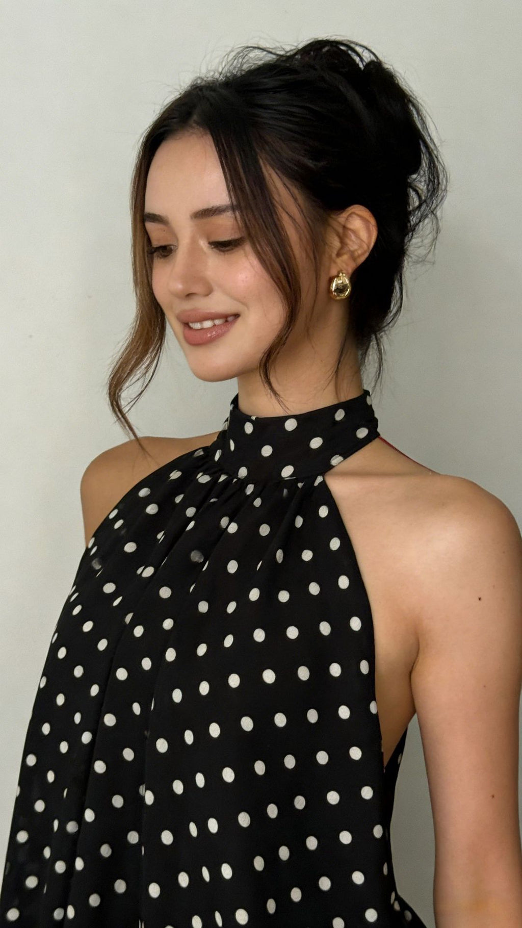Woman wearing a black polka dot halter top against a plain background