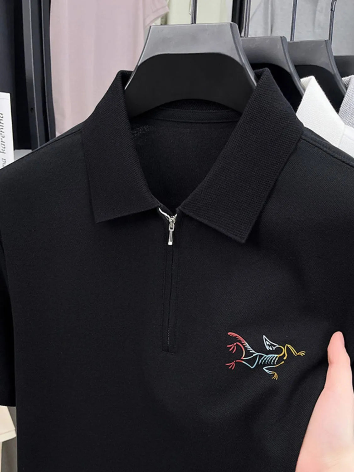 Black polo shirt with a colorful embroidered design on a hanger-blackorvani.com