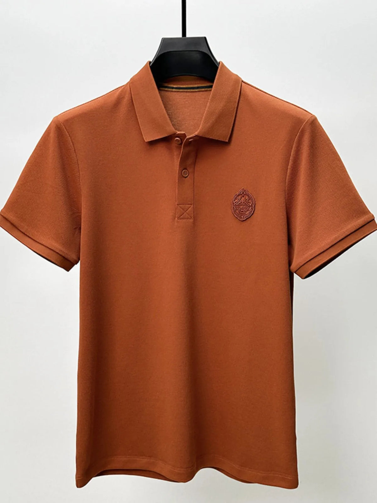 Brown polo shirt with a logo on a hanger against a white background