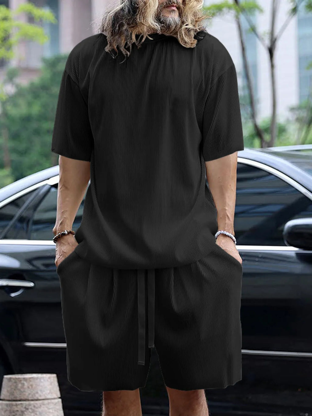 Person wearing a black outfit standing in front of a car with a blurred background