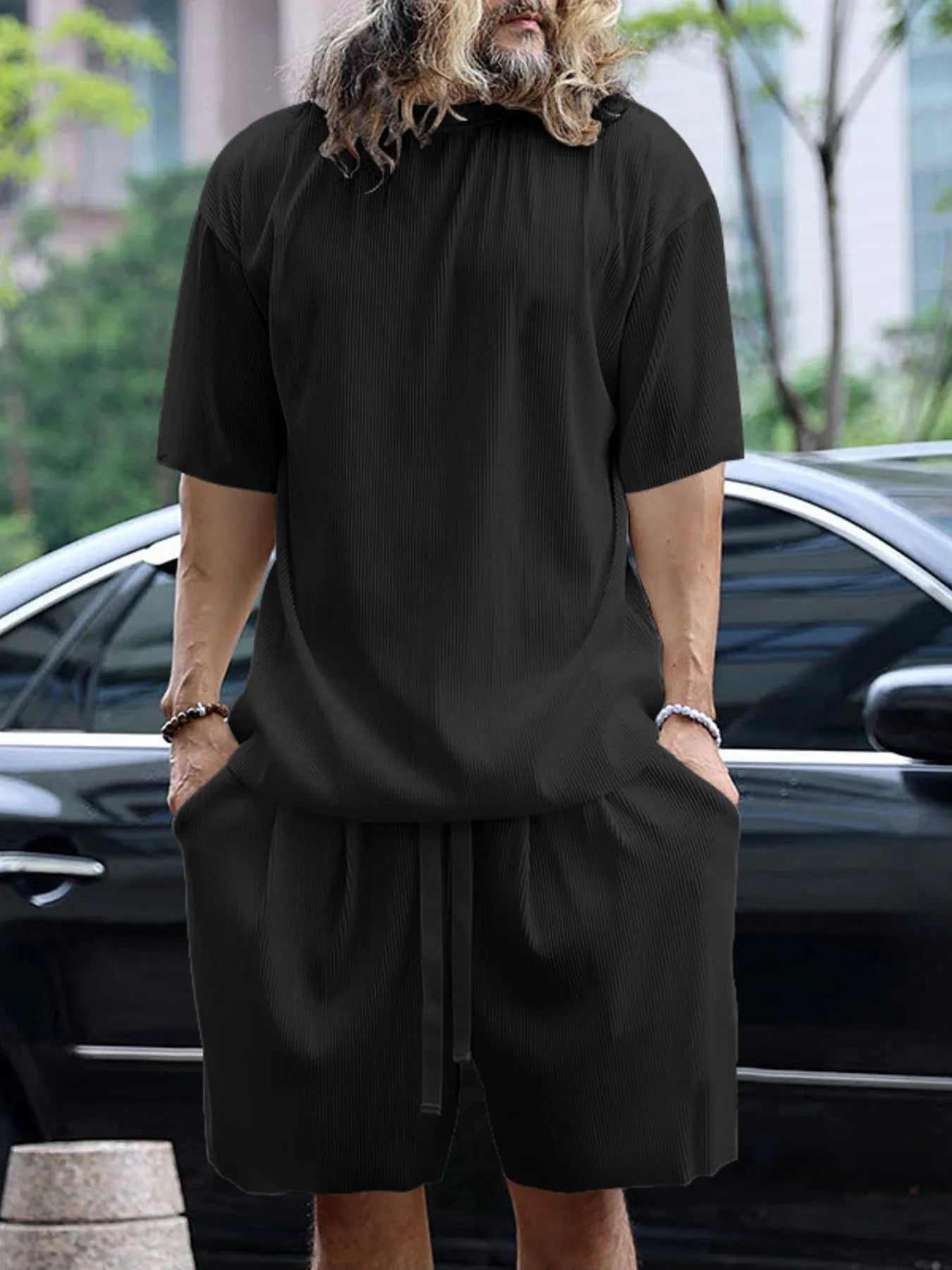 Person wearing a black outfit standing in front of a car with a blurred background