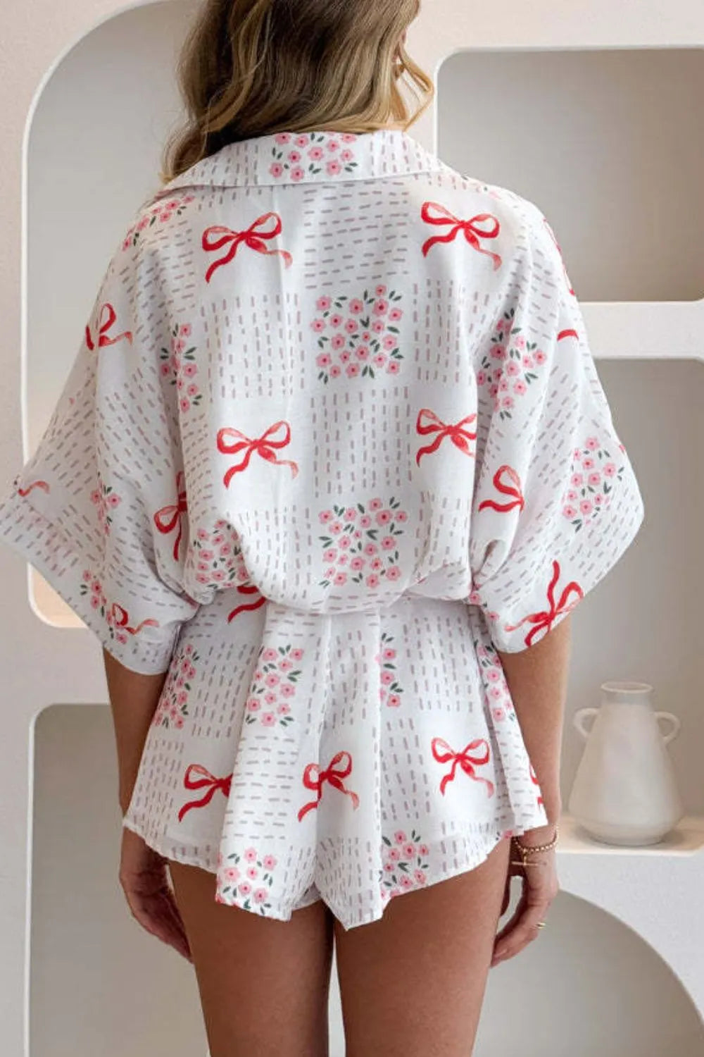 White outfit with red bow pattern worn by a person, standing against a neutral background-BlackOrvani