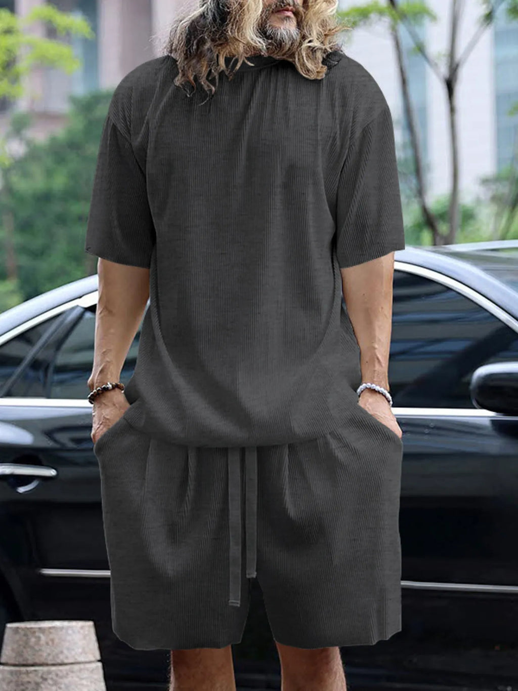 Person wearing a dark gray outfit with a car and trees in the background