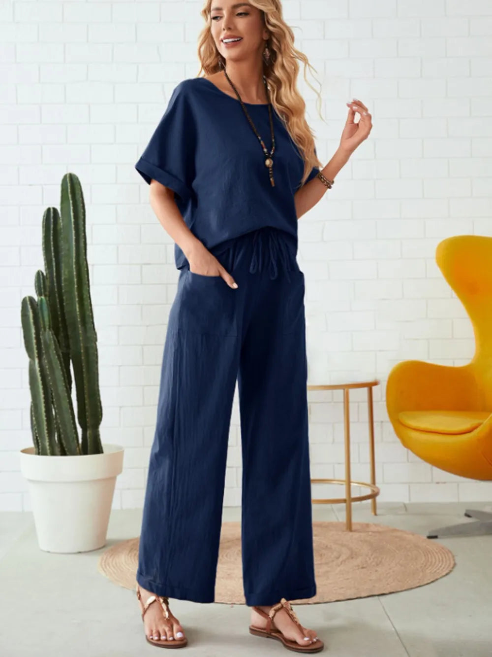 Woman wearing a navy blue outfit standing in a room with a cactus and yellow chair-blackorvani