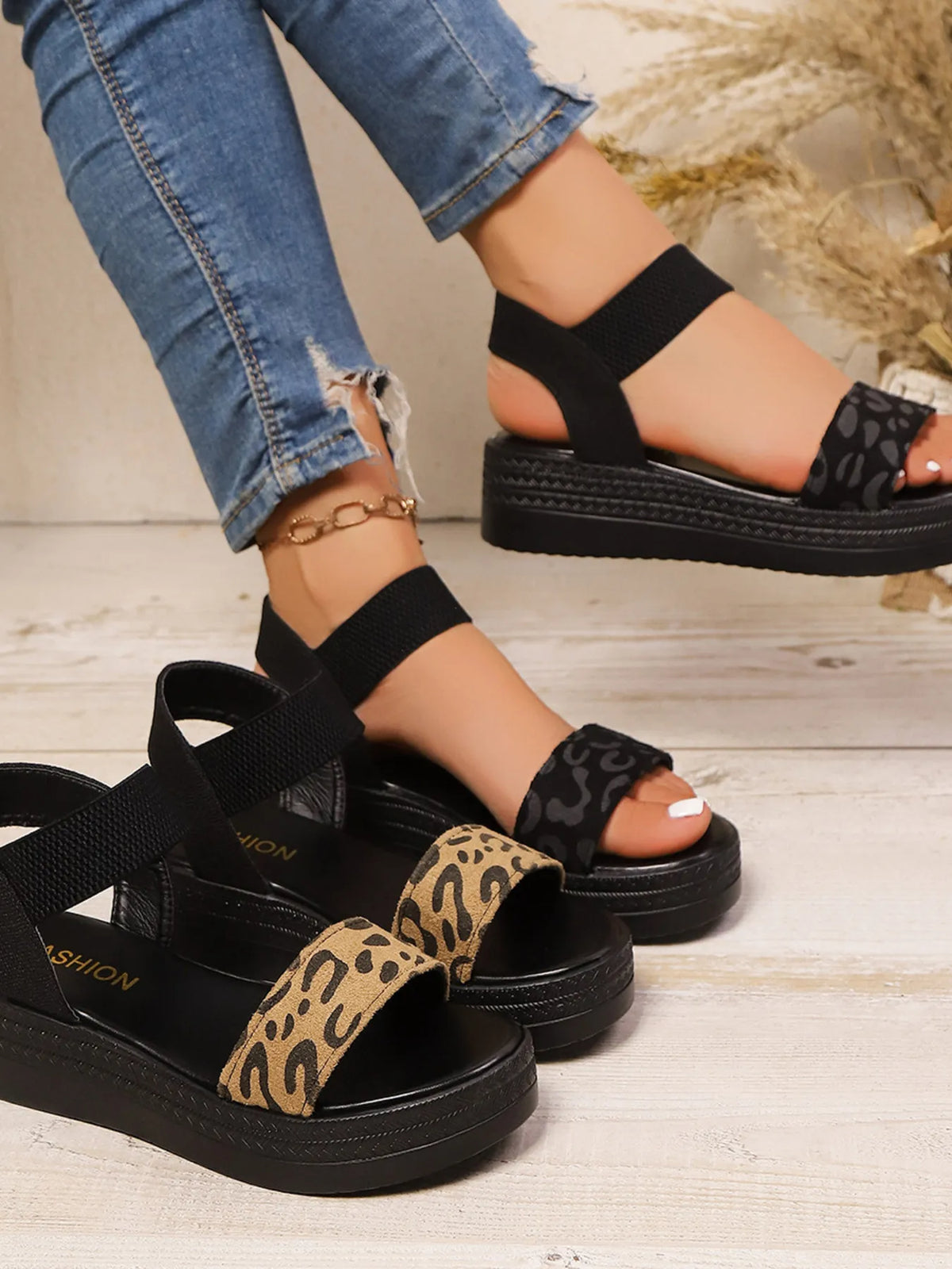 Black sandals with leopard print straps worn with ripped jeans on a wooden floor.