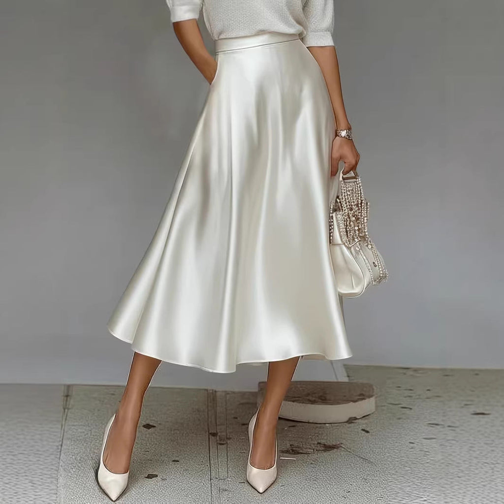 Person wearing a white satin skirt with beige high heels and a patterned handbag on a neutral background