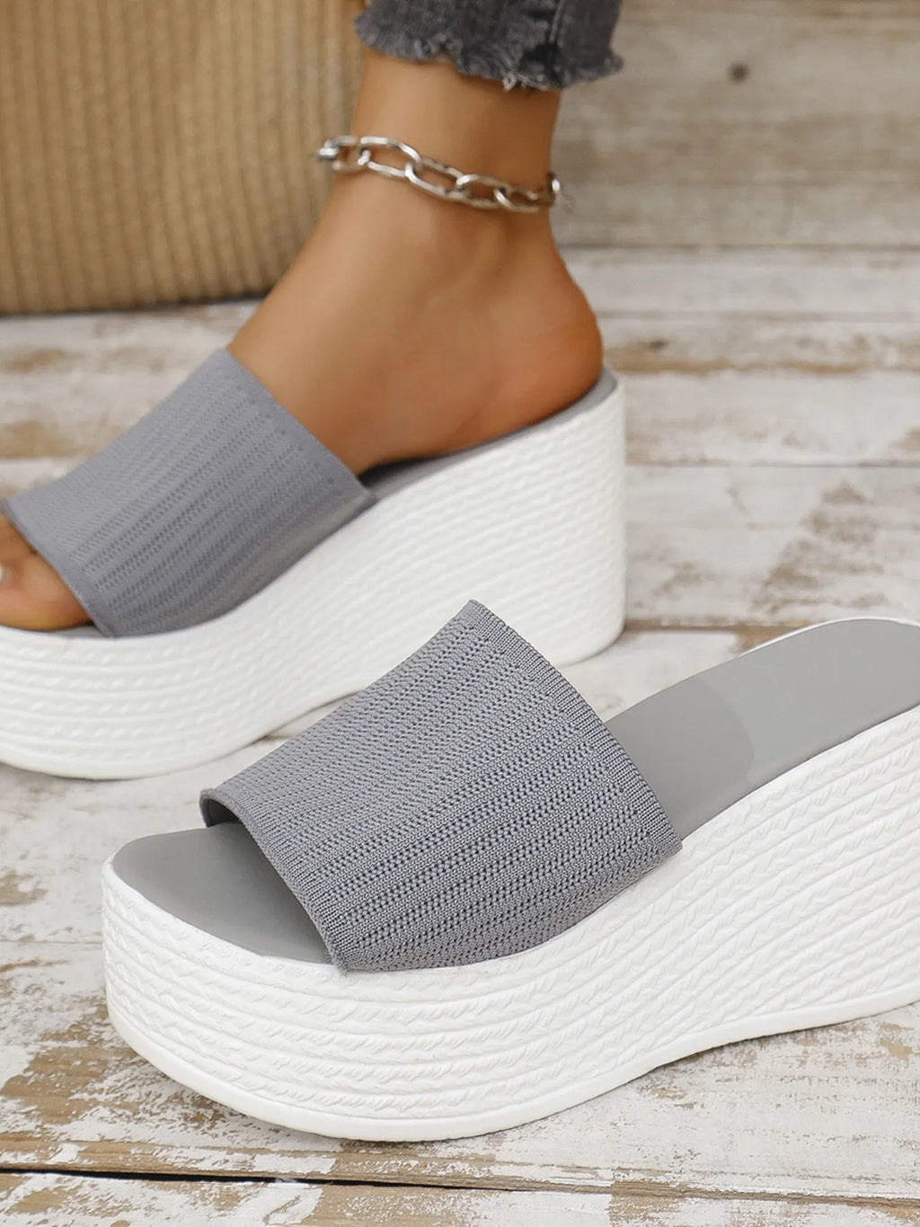 Gray sandals with white soles worn by a person on a wooden floor.
