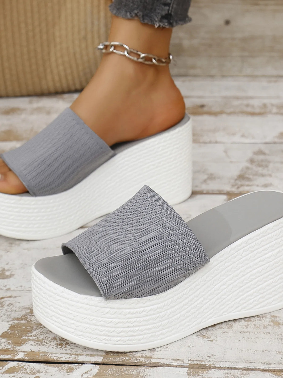 Gray sandals with white soles worn by a person on a wooden floor.