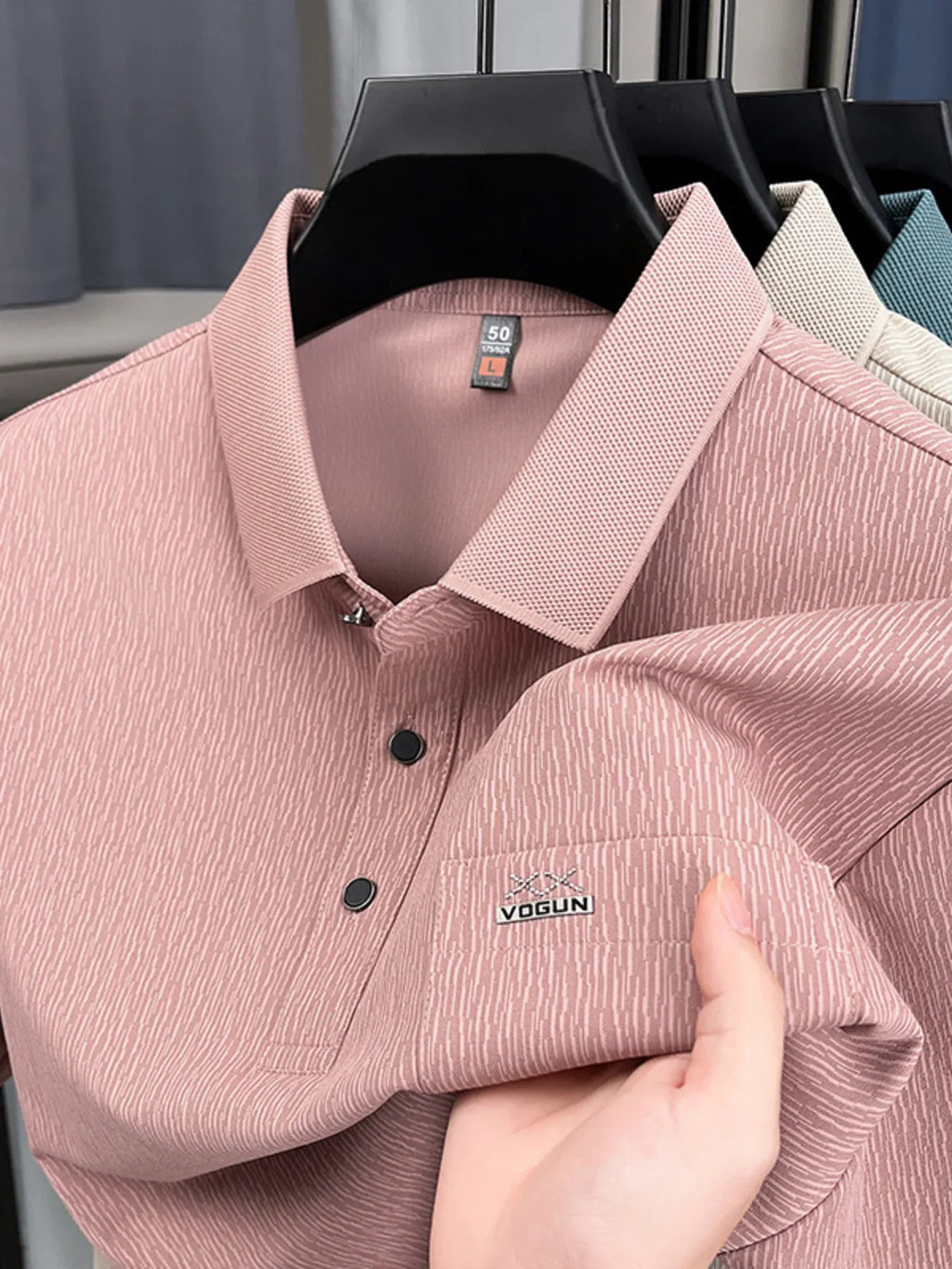 Pink polo shirt with Yagun logo held by a hand, hanging shirts in the background-blackorvani.com
