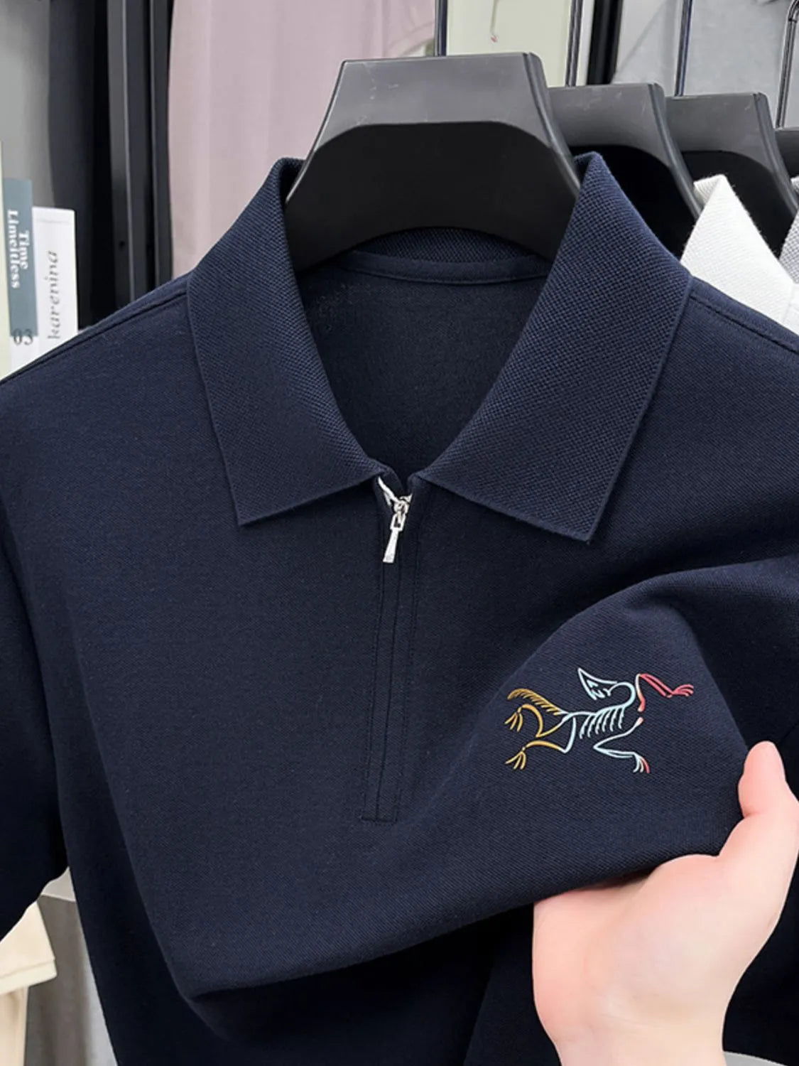 Navy blue polo shirt with embroidered design on sleeve, held by a hand-blackorvani.com