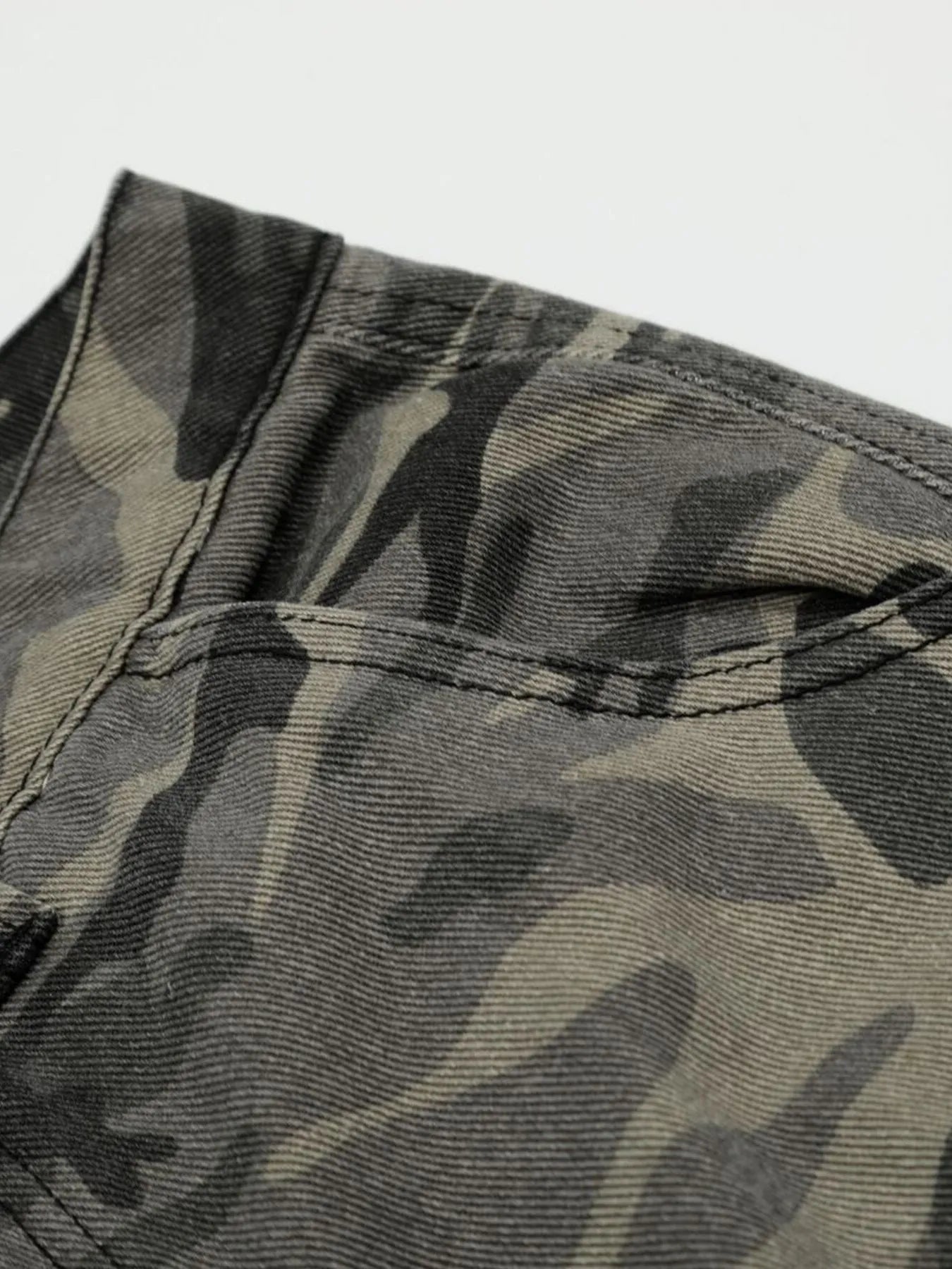 Close-up of camouflage-patterned fabric with a visible stitching detail on a light gray background-Black Orvani