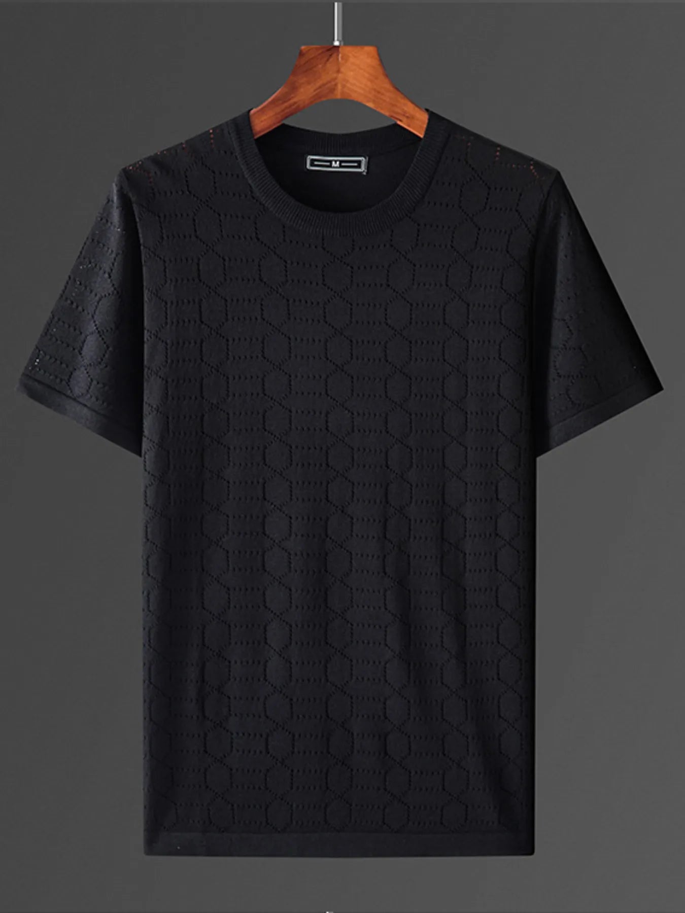Black textured t-shirt on a wooden hanger against a dark background