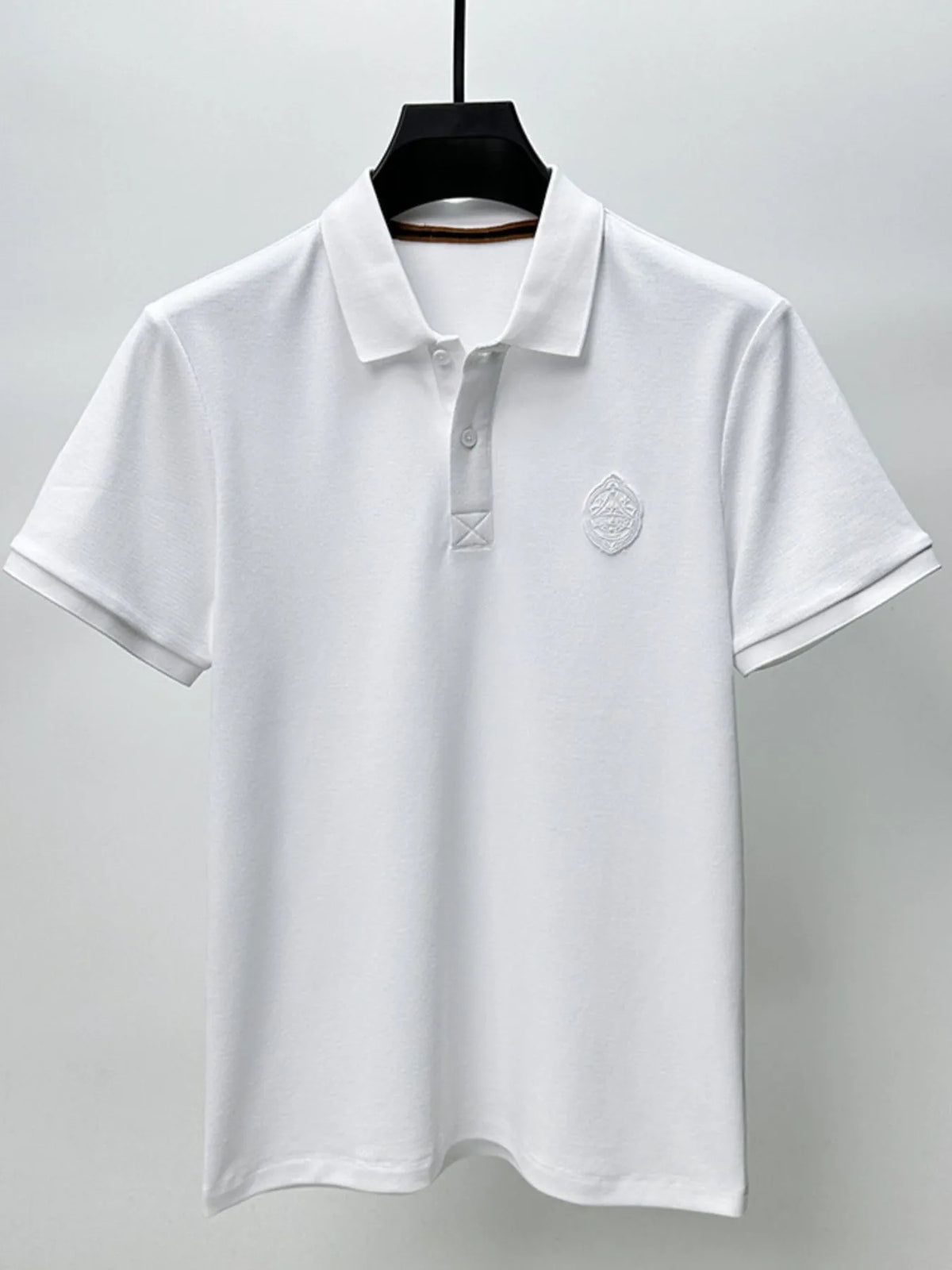 White polo shirt with a logo on a hanger against a gray background