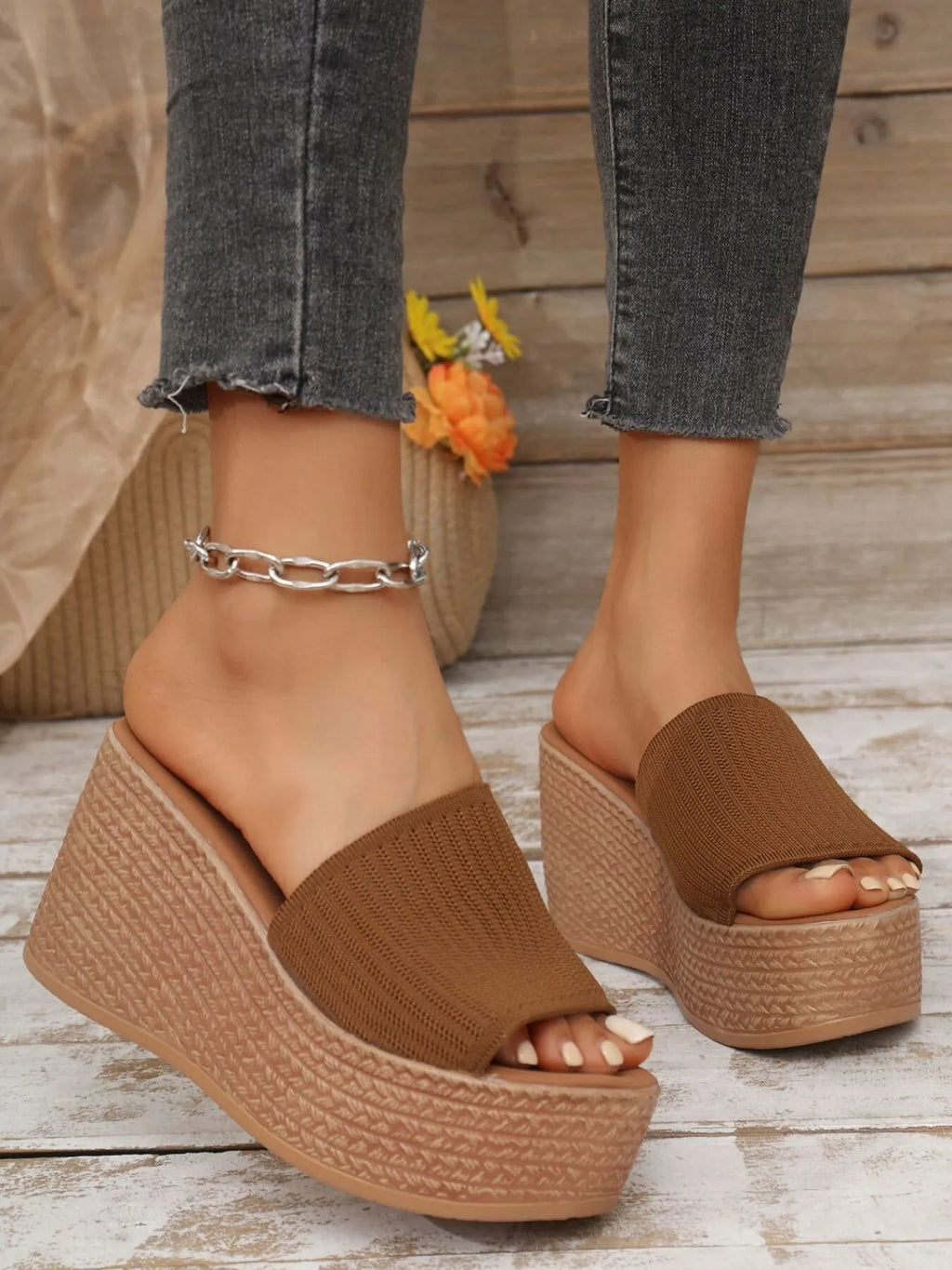 Brown wedge sandals worn with gray jeans on a wooden floor.