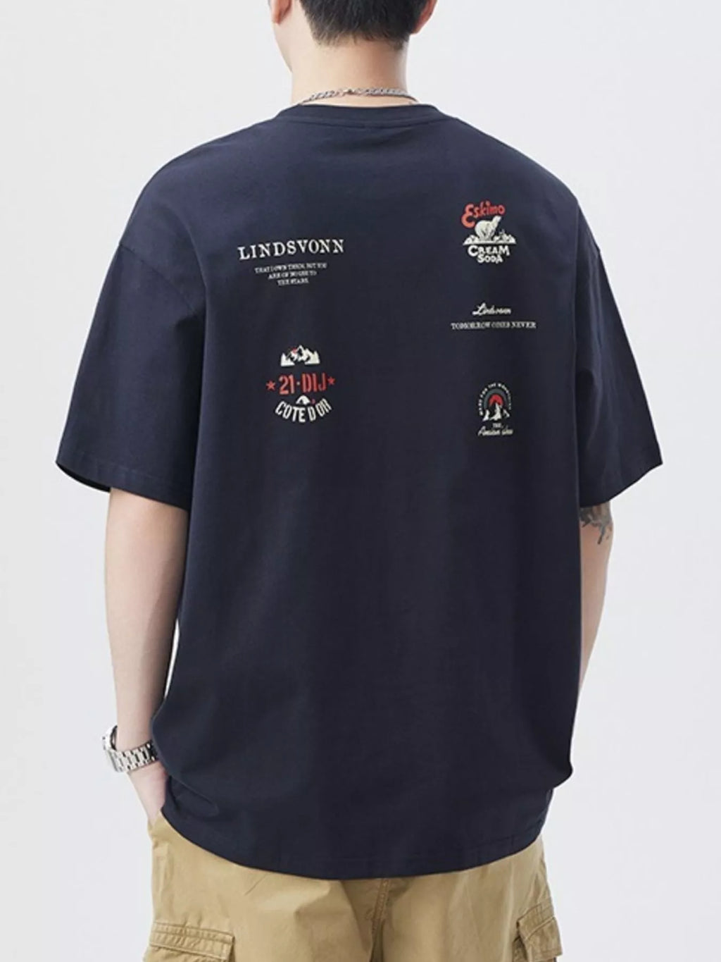 Person wearing a navy blue t-shirt with multiple logos on the back against a plain background-blackorvani.com