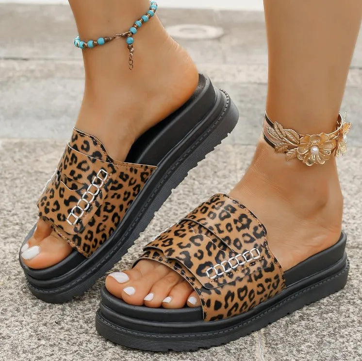 Leopard print sandals with black platforms worn on feet with anklets.