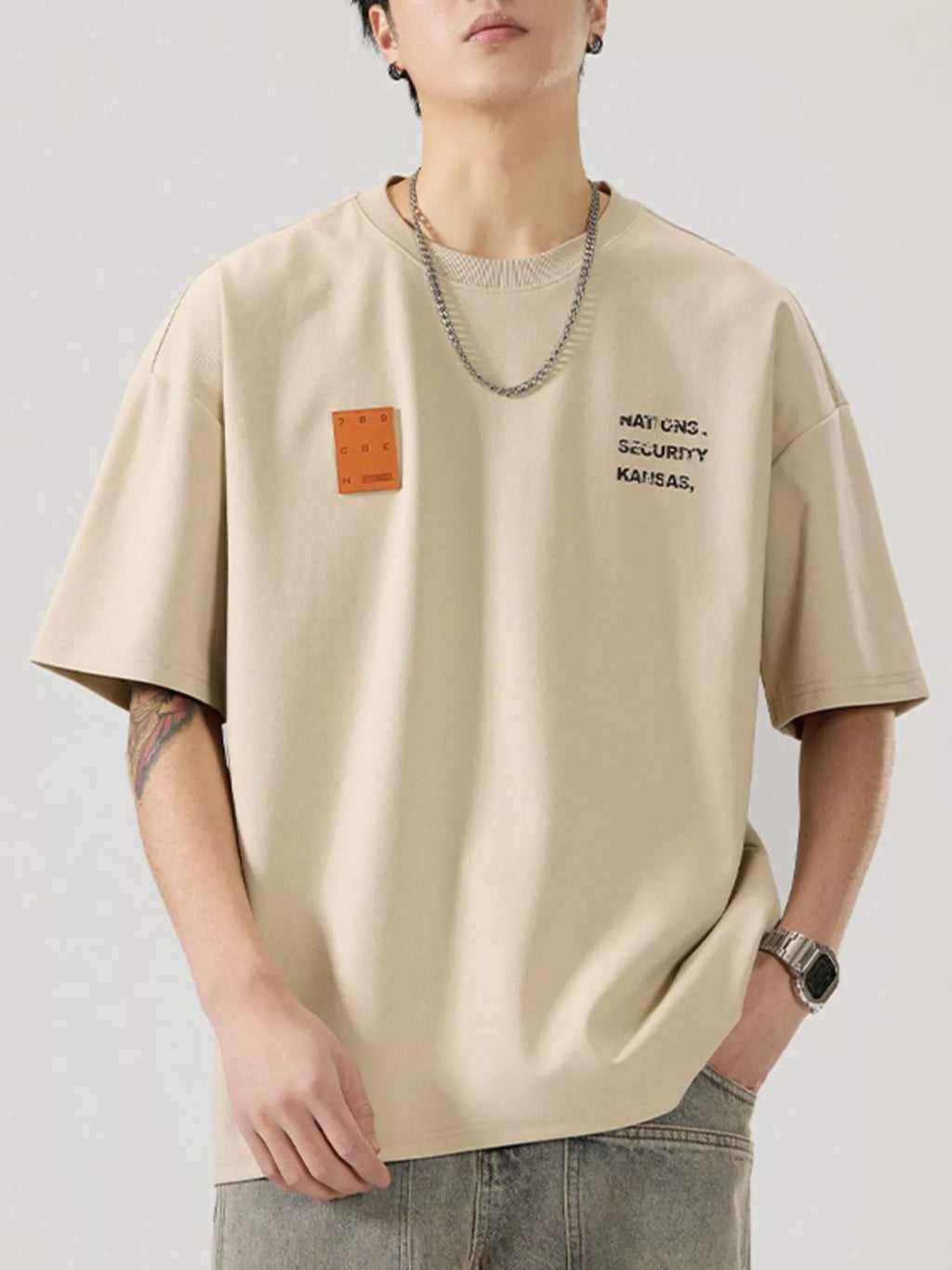 men wearing a beige t-shirt with text and a patch on a plain background