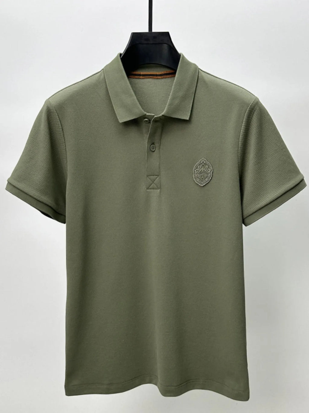 Green polo shirt with a logo on a hanger against a white background