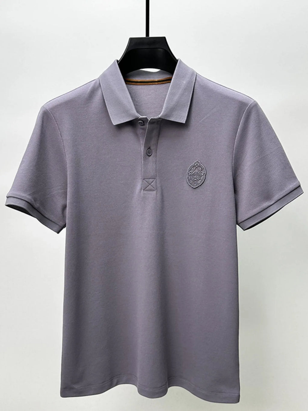 Gray polo shirt with a logo on a hanger against a white background