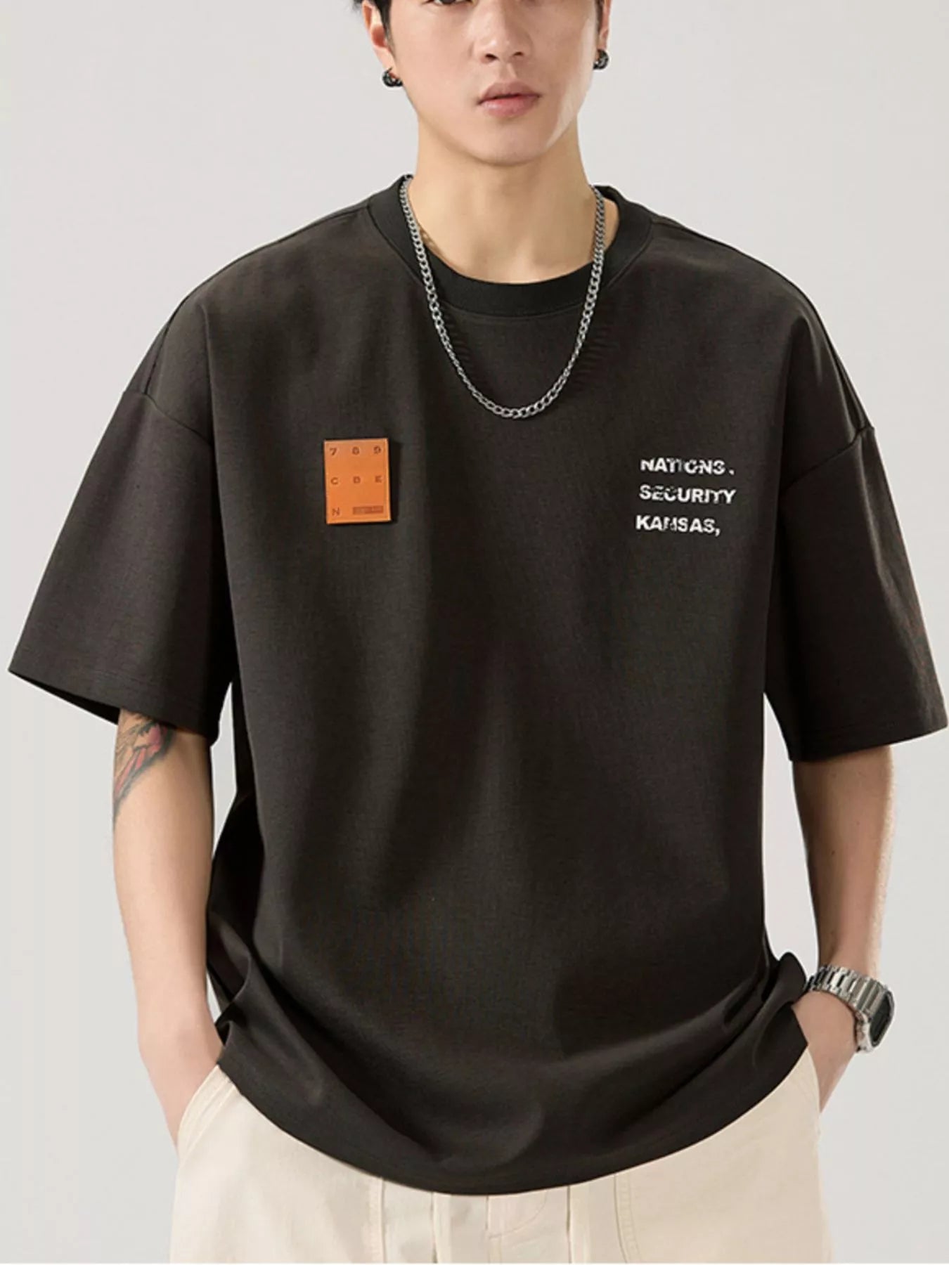 men wearing a black t-shirt with text and a patch on a plain background