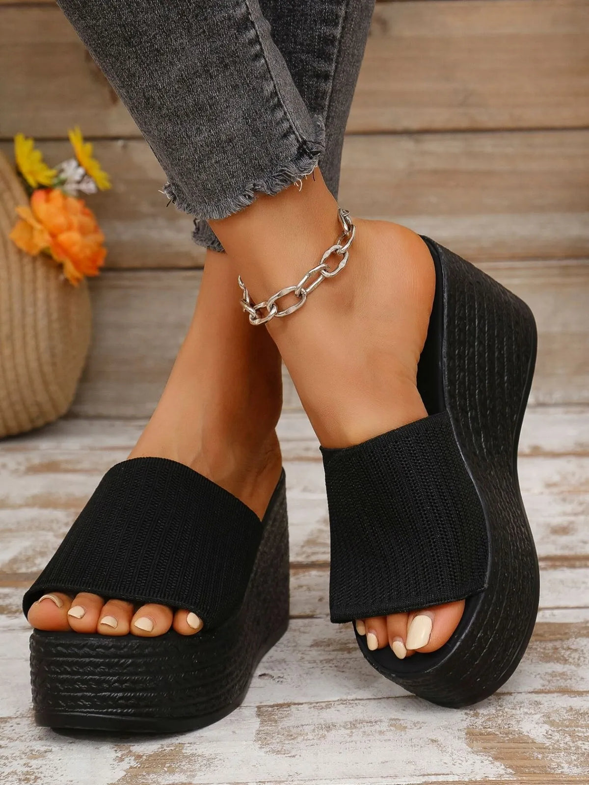 Black platform sandals worn with gray jeans on a wooden floor.