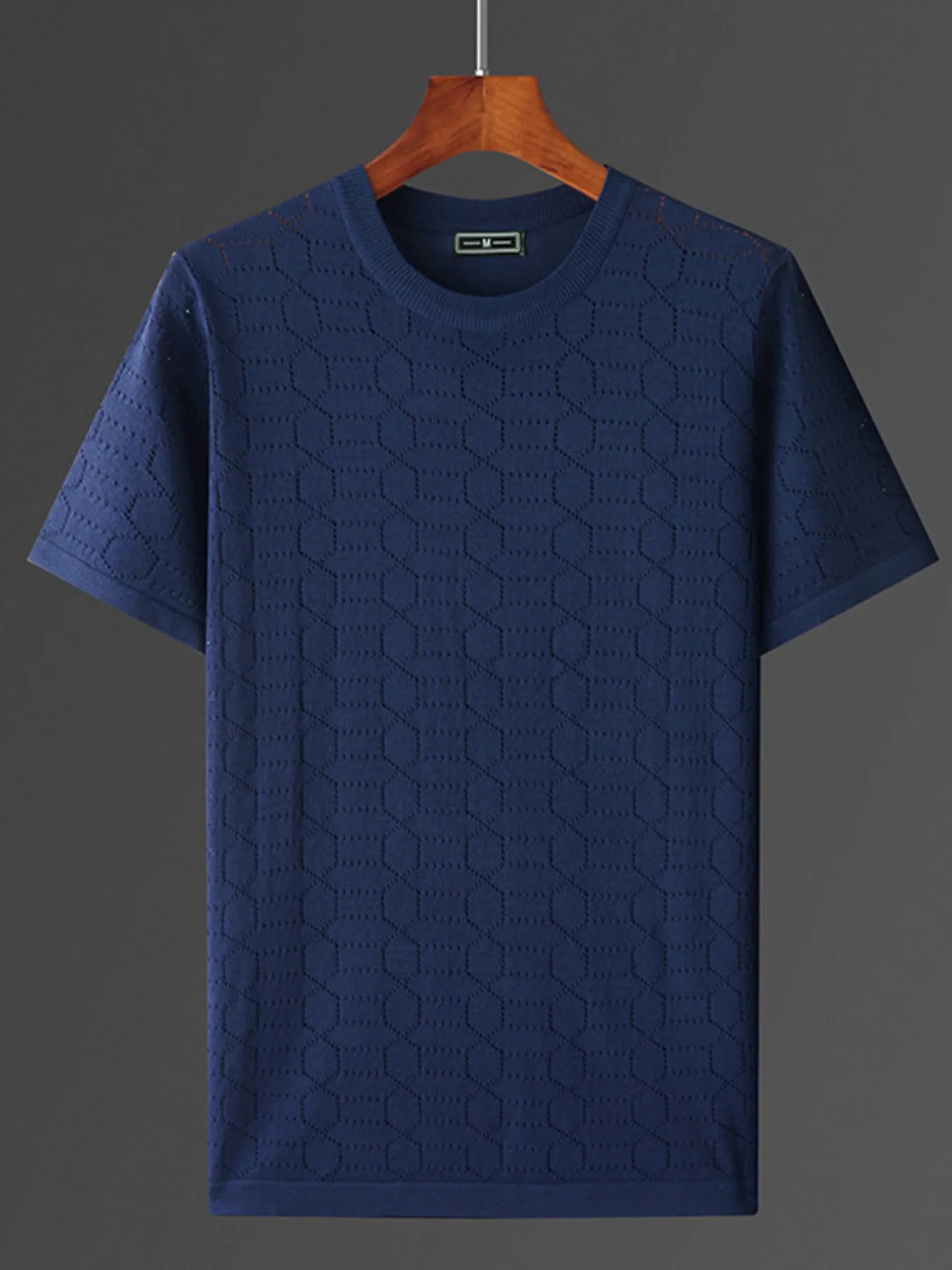 Blue textured t-shirt on a wooden hanger against a dark background