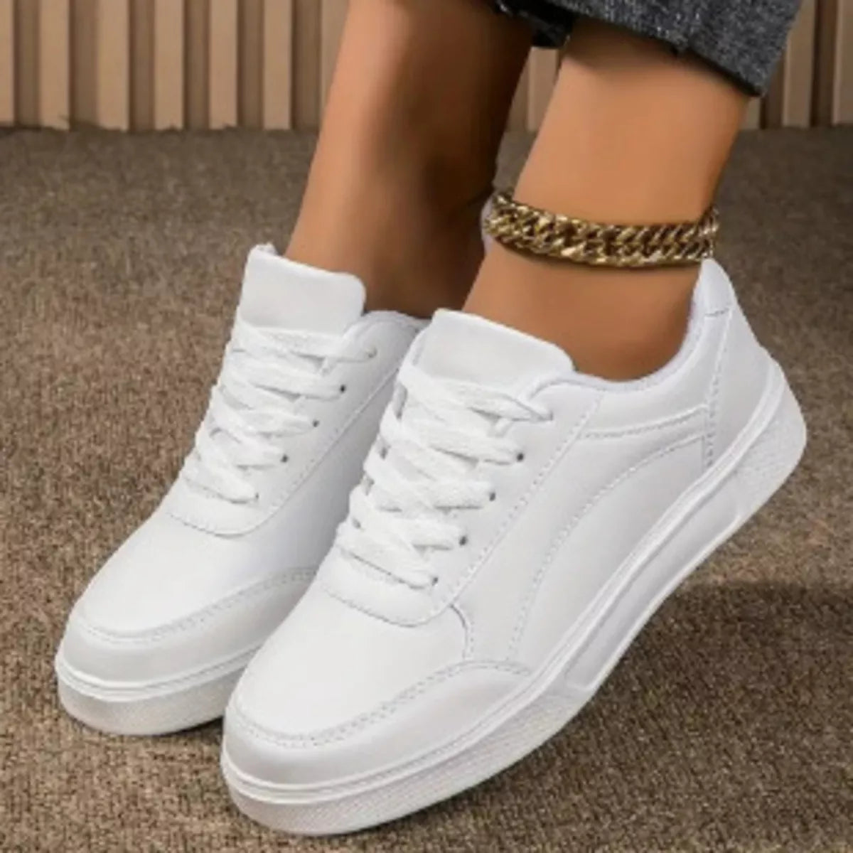 White sneakers worn on a brown carpet with a gold chain bracelet-blackorvani.com