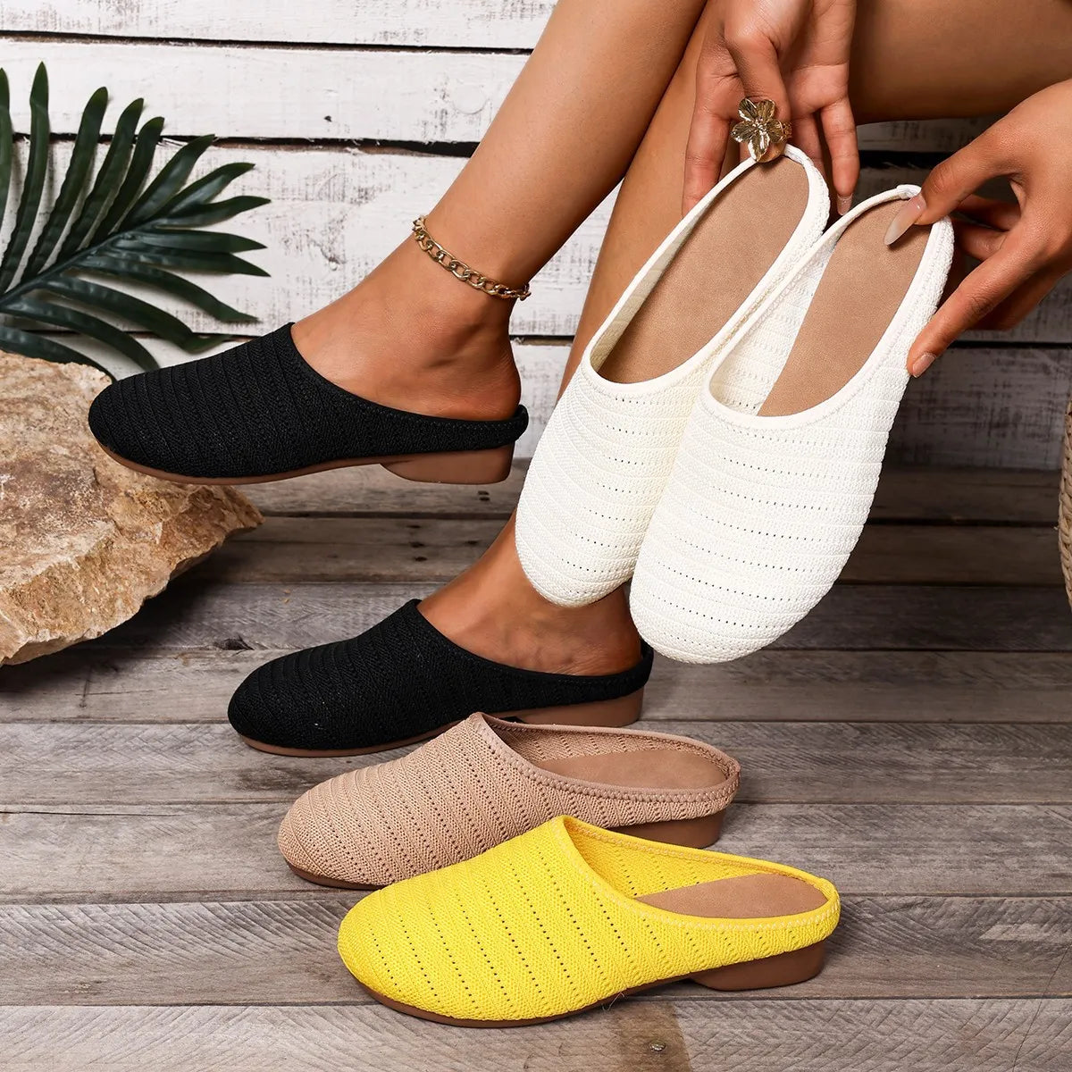 Four pairs of slippers in black, white, beige, and yellow on a wooden floor.