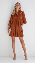 A woman modeling a rust-brown short dress with balloon sleeves and a buttoned neckline, standing against a plain light gray studio background-blackorvani